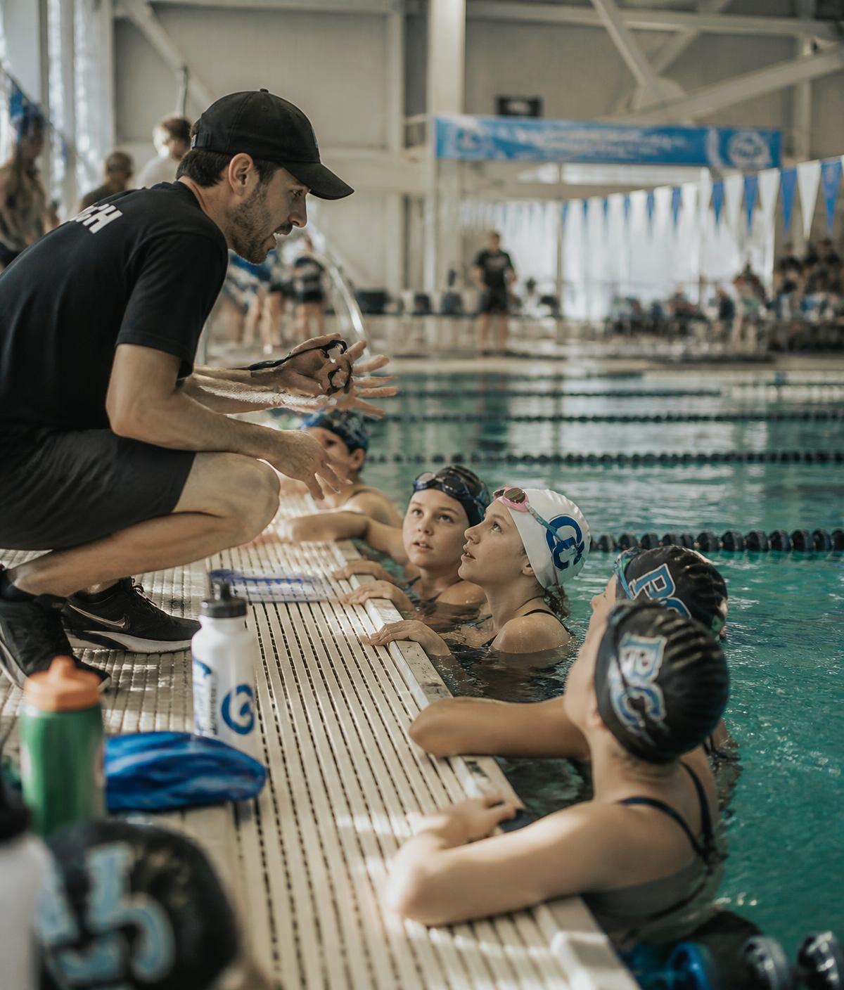 Coach speaking with young swimmers at the wall during practice